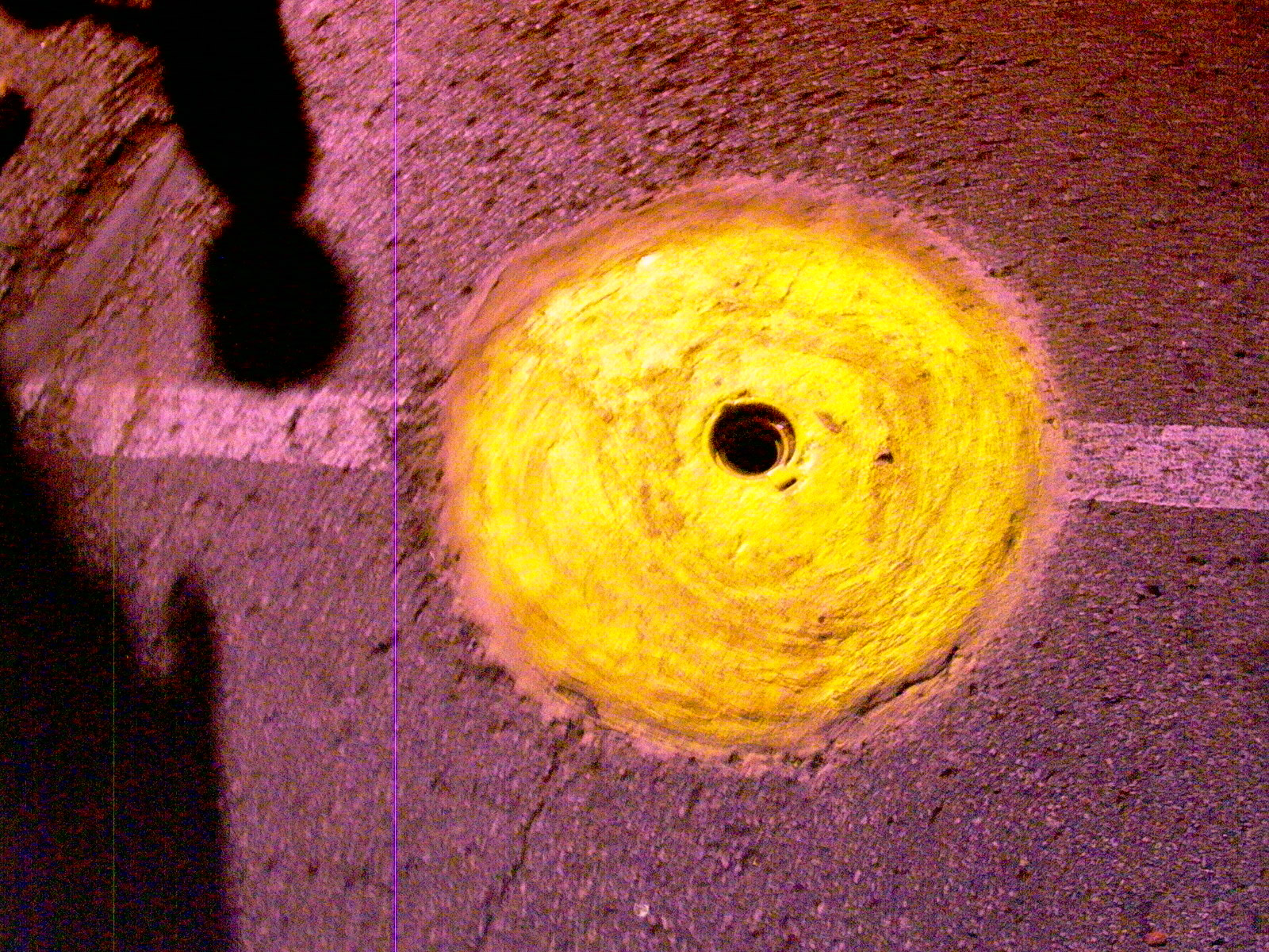 A glowing yellow circle of sealant on night asphalt, a long shadow falling across it