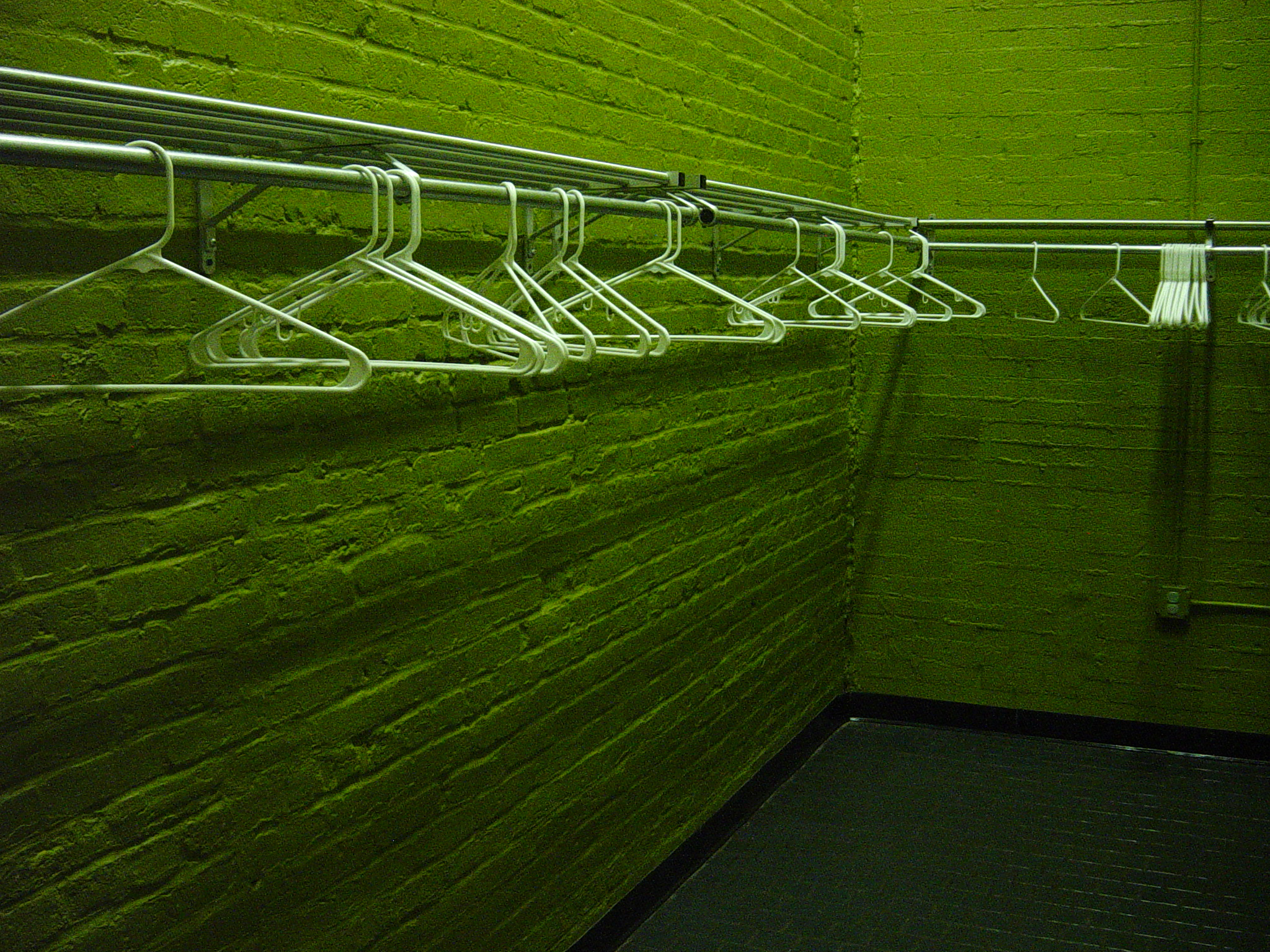 White wire hangers lined across a wall washed in green light, their shadows repeating into the dark