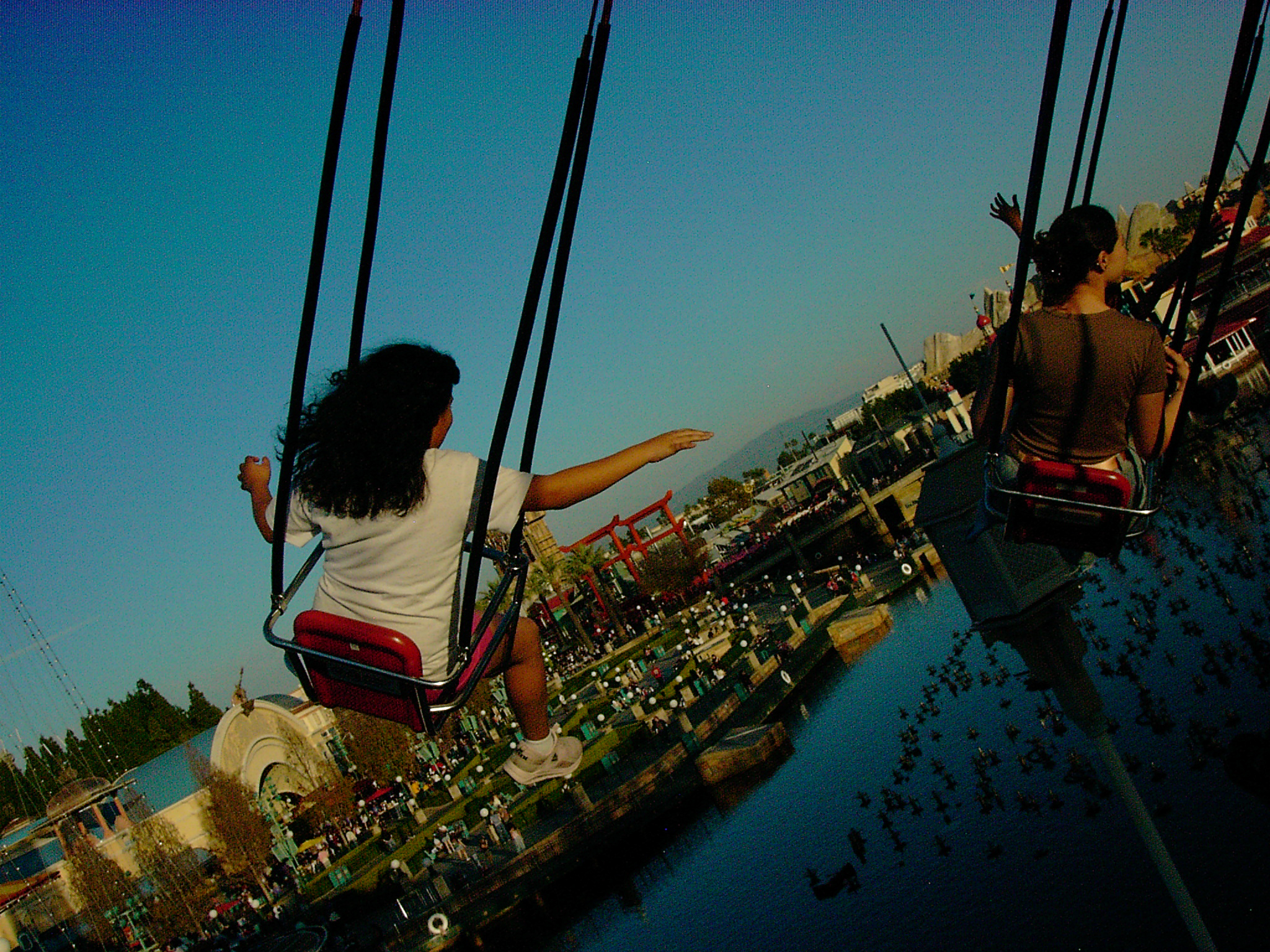 A tilted fair ride swing at sunset, riders suspended against metal arms and a green-blue sky